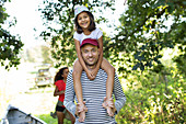 Portrait father carrying daughter on shoulders in woods