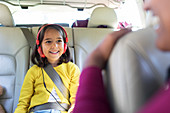 Smiling girl with headphones riding in back seat of car