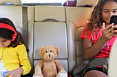 Sisters with teddy bear in back seat of car