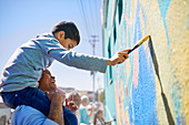 Father and son volunteers painting mural on wall