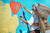 Senior couple painting heart-shape mural on wall