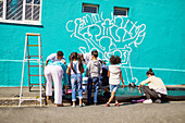 Kid volunteers painting community mural on wall