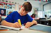 Focused school boy student using highlighter, doing homework