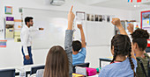 school students with hands raised during lesson