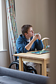 Thoughtful woman in wheelchair drinking tea