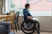 Thoughtful woman in wheelchair looking out window