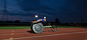 Young paraplegic athlete in wheelchair race at night
