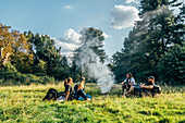 Friends camping, relaxing around campfire in field