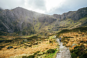 Woman walking along craggy mountain trail, Snowdonia NP, UK