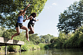 Carefree mother and daughter jumping into river