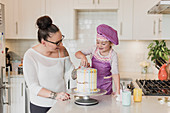 Mother and daughter decorating cake in kitchen