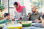 Mother in hijab serving dinner to family at table