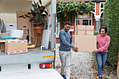 Couple moving out of house, carrying boxes to moving van