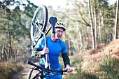 Male cyclist carrying bicycle on sunny trail in woods