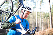 Male cyclist carrying bicycle in sunny woods