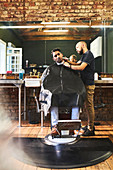 Male barber shaving face of customer in barbershop