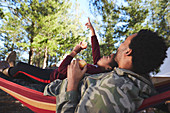 Father and son relaxing in hammock below trees in woods