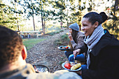 Happy friends eating at campsite in woods