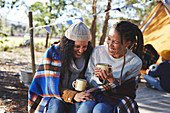 Lesbian couple laughing, drinking coffee at campsite