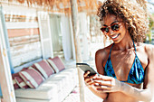 Happy young woman using smart phone on beach hut patio