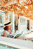 Woman reading book on beach hut patio