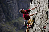 Male rock climber scaling rock face, looking up