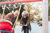 Grandparents pushing toddler on swing at playground