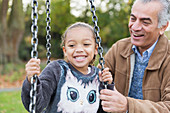 Playful grandfather and granddaughter on playground swing