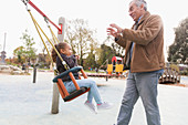 Grandfather pushing granddaughter on playground swing