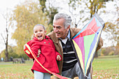 Playful grandfather and granddaughter flying a kite