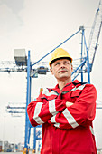 Confident dock worker below crane at shipyard