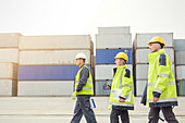 Dock workers walking along cargo containers at shipyard