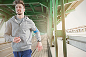 Young male runner running along urban train tracks