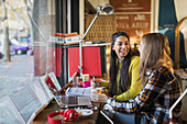 Smiling female college students studying at cafe window