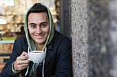Portrait young man drinking coffee at sidewalk cafe