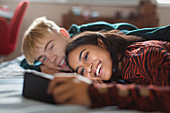 Smiling teenage couple using smart phone on bed