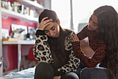 Teenage girl comforting upset friend on bed