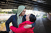 Happy, young couple hugging under urban bridge