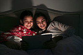 Girls watching movie on digital tablet in dark bedroom