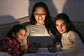Mother and daughters using digital tablet in dark bedroom
