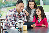 Happy father and daughters using tablet in morning kitchen