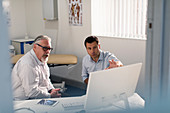 Male doctor meeting with senior patient at computer