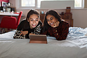 Happy teenage girls using digital tablet on bed