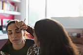 Teenage girl applying eyeshadow makeup to friends eye