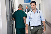 Male doctor with tablet walking in hospital corridor