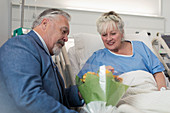 Senior man bringing flower bouquet to wife resting