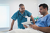 Nurse talking with patient using tablet in hospital bed
