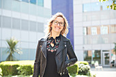 Portrait woman in leather jacket outside sunny building