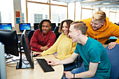 Happy college students using computer together in library