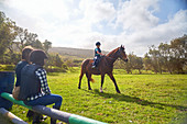 Girl horseback riding in sunny grass paddock